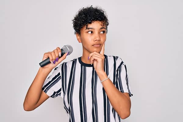 Beautiful african american afro singer woman singing using microphone over white background serious face thinking about question, very confused idea
